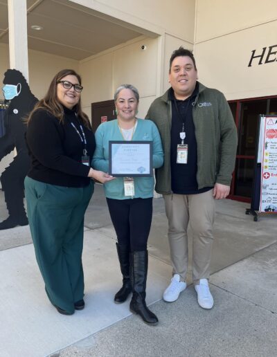 Three people standing outside a building holding a community partner recognition certificate.