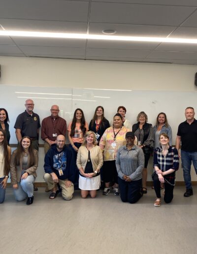 Group of adults posing for a photo in a classroom with a whiteboard behind them.
