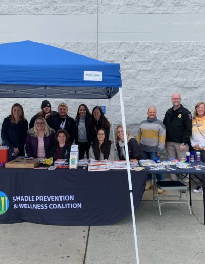 Community group gathered at a Shadle Prevention & Wellness Coalition booth under a canopy outside a store.